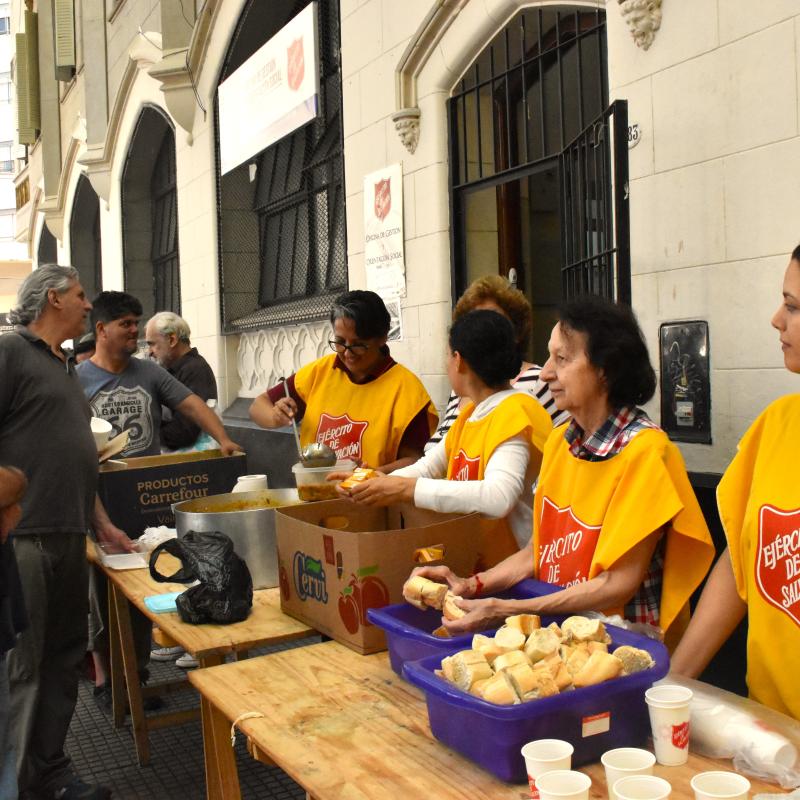 People in Salvation Army tabards serve soup from tables in the street