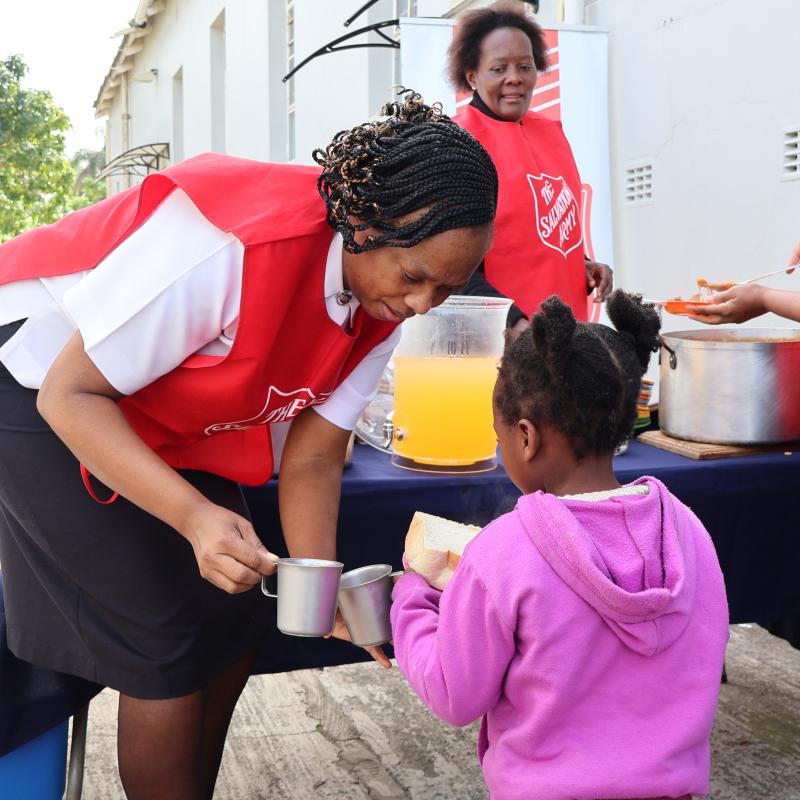 A woman in Salvation Army uniform taps mugs with a little girl