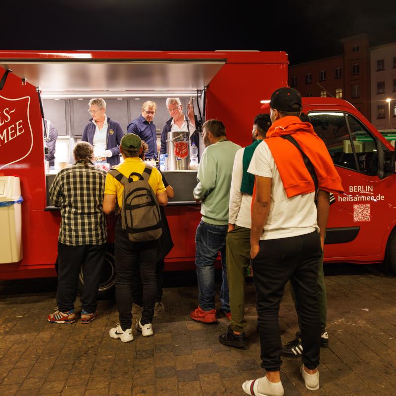 People queue for food in front of a red Salvation Army van