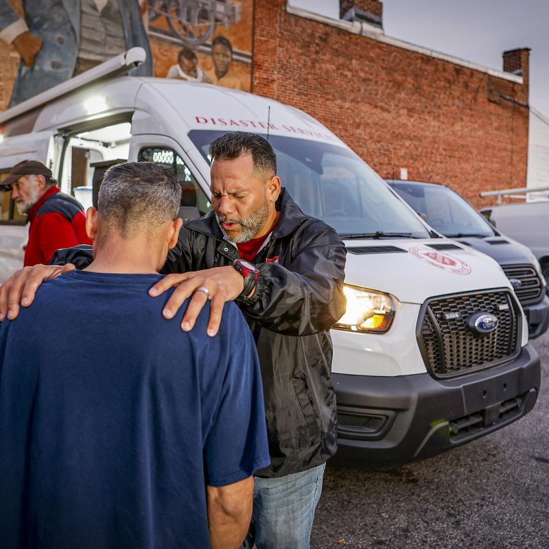 Two men pray in front of a Salvation Army emergency vehicle