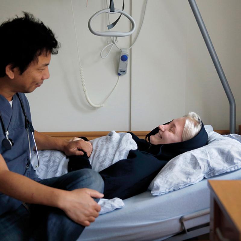 A man in medical uniform speaks to a patient in a hospital bed