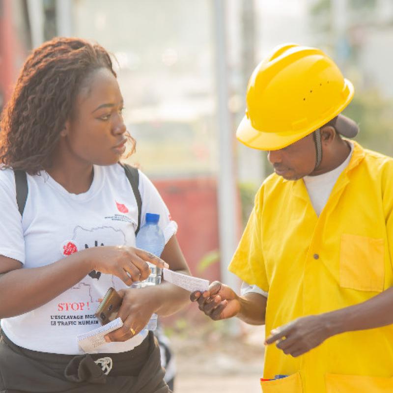 A woman in a Salvation Army t-shirt hands a flyer to a man on the street