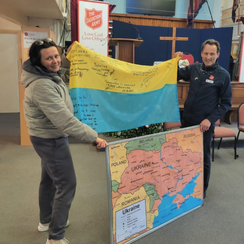 A woman and a man in Salvation Army uniform hold a Ukrainian flag and a map of the region