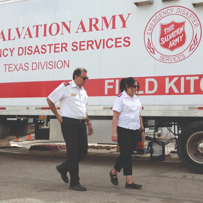 Two people in Salvation Army uniform walk past a field kitchen