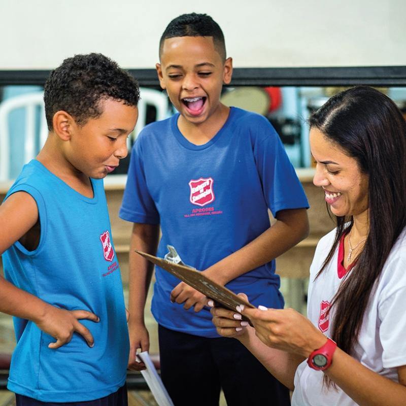 Children in Salvation Army t-shirts laugh together as a volunteer checks a clipboard