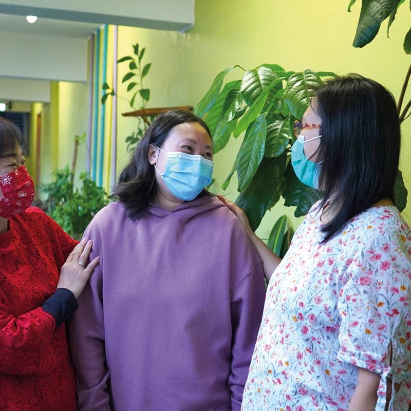 Three women, wearing facemasks, chat together