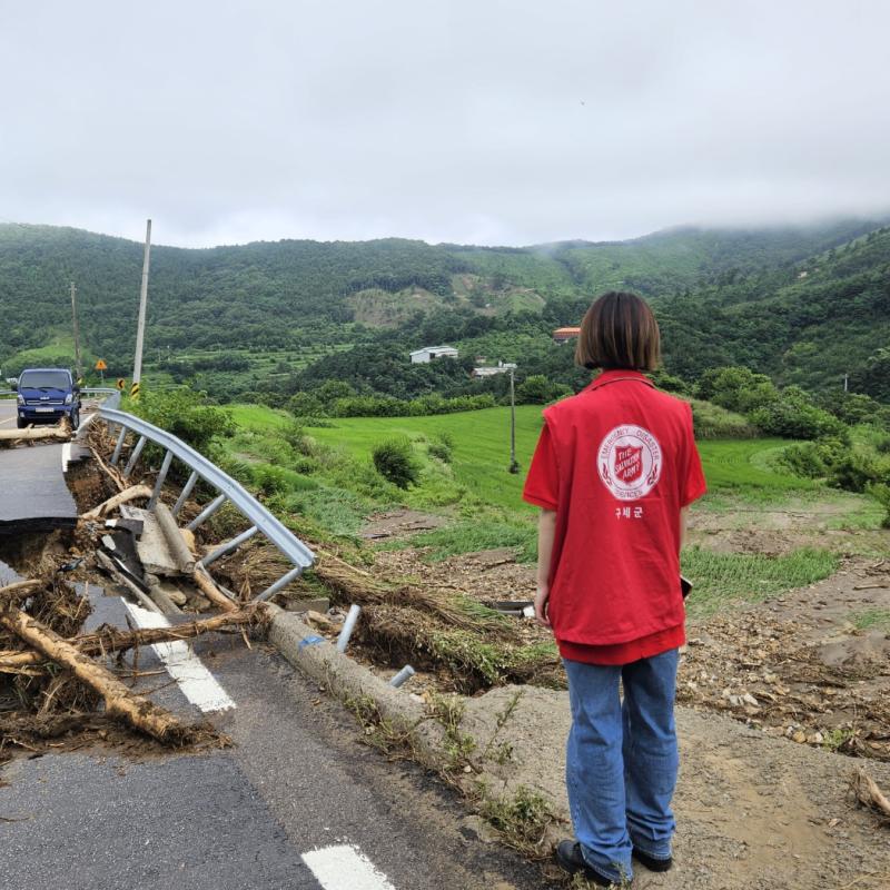 A person in a Salvation Army t-shirt looks out at a flood-damaged road